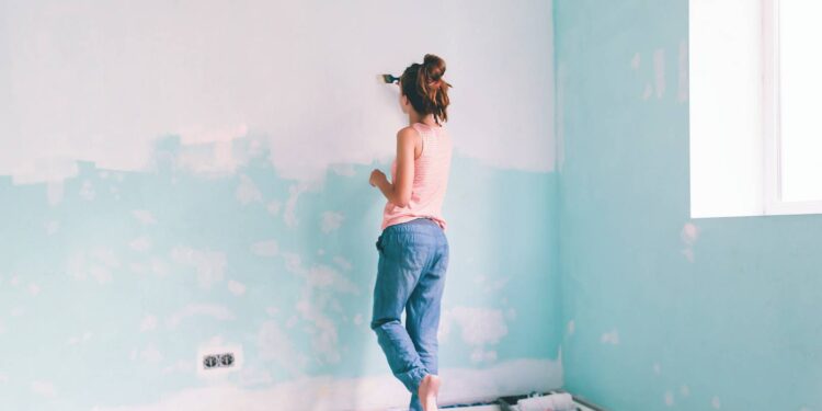 Kobieta maluje pędzlem ścianę w pokoju